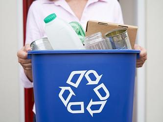 woman holding blue recycling bin filled with empty tins, cardboard and other food containers